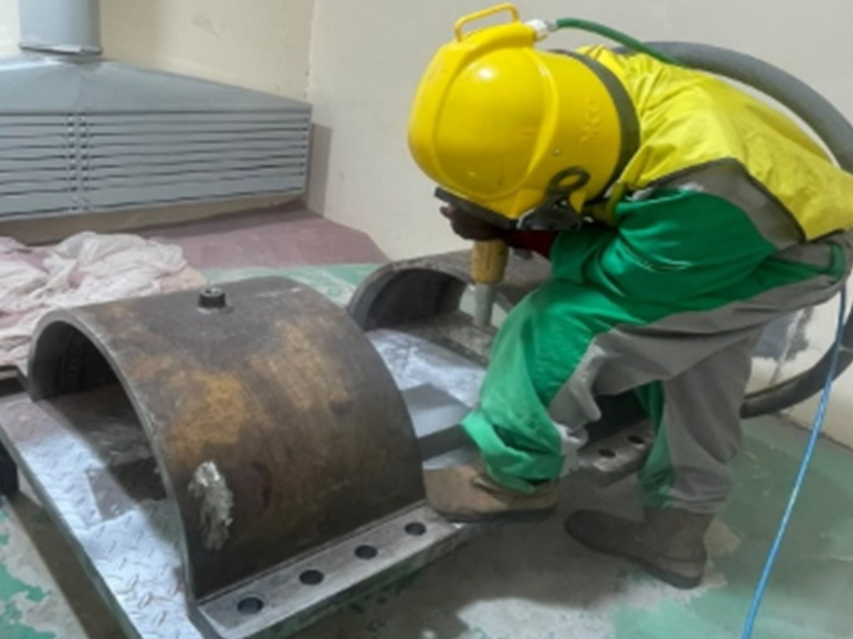 Operator blasting a steel component before painting